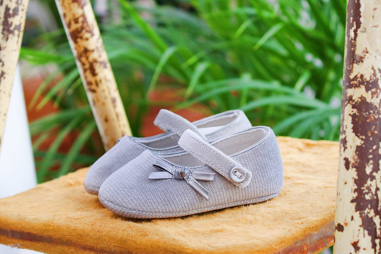 Adorable gray baby shoes with bows on a rustic chair backdrop, surrounded by greenery.